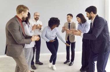 Afrika kökenli Amerikalı bir kadın, toplantı sırasında alkışlayan meslektaşlarından oluşan bir ekiple bir ofiste dans ediyor ve başarıyı kutluyor. Takım çalışması ve birlik, iş yerinde iş başarısı.