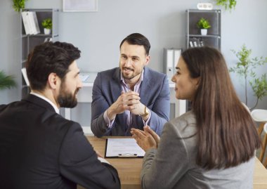 Mutlu çift mali danışmanla görüşüyor, sigorta acentesiyle yasal belge ve anlaşma için görüşüyor. Gülümseyen eş ve koca, ajanstaki danışmanın önünde oturuyor. Anlaşma kavramı