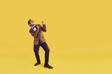Sarı renkli reklam metinlerinin arka planında mutlu komik adam. Moda leopar ceketli, papyonlu, dans eden ve bir şeye bakan neşeli, etnik bir gencin tüm vücudunu çekiyoruz.