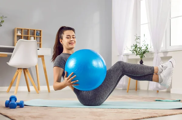 Evdeki formda topla yoga minderinin üzerinde uzanarak formda egzersizler yapan neşeli genç bir kız. Spor yapan, gülen bir kadın, içeride sağlık için egzersiz yapıyor. Sağlıklı yaşam tarzı, spor ve spor anlayışı.
