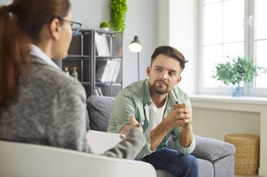 Psikolog ve erkek danışmanı, terapi seansında koltukta oturan düşünceli bir hasta profesyonel kadın danışmana bakmak, güvenle psikoterapi rehberliği dinlemek.