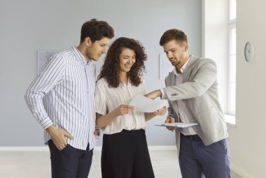 Birkaç belge ve ev turu sözleşmesi gösteren bir emlakçı. Müşteriler ve borsacılar satın alma seçenekleri ve şartları tartışmak için boş odada duruyorlar, yatırım planı ve emlak anlaşmasını onaylıyorlar