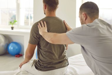 Erkek osteopat modern ofiste genç bir adamı muayene ediyor. Genç fizyoterapist rehabilitasyon kliniğinde tedavi görüyor. Kayropraktik uzmanı omurga eğriliği ve sırt ağrısı olan hastaya yardım ediyor..