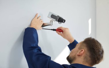 Teknisyen ofis duvarına ya da evin içine güvenlik kamerası yerleştiriyor. Erkek elektrikçi, suç ya da rüşvet tespiti için CCTV sistemi kuruyor. Modern teknoloji kavramı.