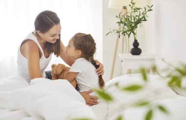 Mutlu aile sabahı, genç anne ve tatlı küçük kız gülümseme sıcak beyaz yorganla kaplanmış gülüş, gülümseyen anne yatak odasındaki battaniyenin altında küçük tatlı bir kız çocuğu ile eğleniyor.