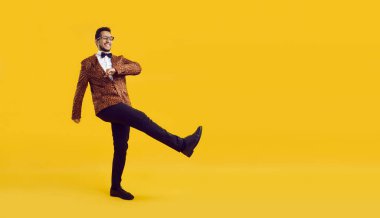 Mutlu komik adamın tam boy stüdyo çekimi. Sarı renkli reklam metninin arka planında saklanmış papyonlu ve gülümseyen abartılı leopar desenli ceketli neşeli genç adam.