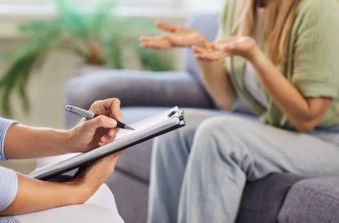 Terapi danışmanı ve destek terapisi seansı. Yakın plan, psikologun müşteri koltukta el kol hareketleriyle empatiyi vurguladığı notlar aldığını gösteriyor. Ruh sağlığı, rehberlik, güven ve destek