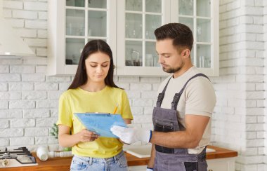 Erkek tesisatçı, kadın müşteriyle evdeki tesisat hizmetleri için sözleşme imzalıyor. Erkek tamirci ya da tamirci kadın müşteri mutfakta bekliyor. Bakım ve onarım servisi.
