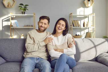 Oturma odasındaki kanepede oturup gülen evli çiftin portresi. Gülümseyen aile babası ve kadın kanepede sarılıyor, sevgi dolu bir eş ve koca. Ahenkli ilişkiler kavramı.