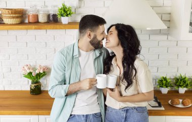 Birbirine aşık çiftler sabah kahvesinin tadını çıkarıyorlar. Romantik ve mutlu bir an, sıradan kotlar giymiş, ayakta duran ve birbirlerine gülümseyerek dokunmak için bardak tutan neşeli bir kadın ve erkek.