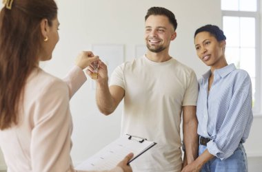 Emlakçı, bir apartman ayini sırasında gülümseyen bir çifte anahtarları veriyor ve yeni sahipleri iç mekanı incelerken satışı tamamlıyor. Emlakçı yeni mutlu ev sahiplerine evin anahtarlarını veriyor.