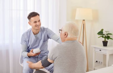 Genç erkek hemşire, klinikteki yaşlı hasta bir hastanın yüksek tansiyonunu ölçüyor. Doktor, yüksek tansiyonu olan yaşlı bir adamın kan basıncını kontrol ediyor..
