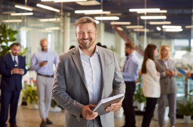 Takım elbiseli, kendine güvenen sakallı iş adamının portresi kişisel ajandası ve kameraya bakıyor. Gülümseyen adam CEO ya da şirket yöneticisi iş dünyasından meslektaşlarının geçmişine karşı.