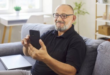 Elinde mutlu bir ifade ve gülümsemeyle cep telefonu tutan son sınıf öğrencisi evinde rahat bir koltukta akıllı telefonuyla oturuyor. Ailesiyle video görüşmesinde gülümseyen, sosyal medyada mesaj atan mutlu yaşlı kişi