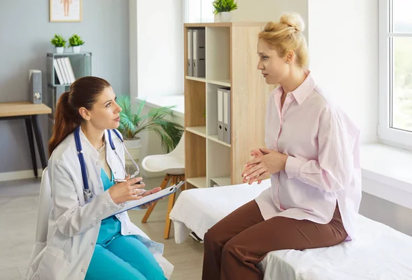 Doktor, bir klinikteki muayene sırasında hastanın semptomlarını anlatırken onu dinler, bir not panosuna not alır ve sağlık hizmeti tavsiyesi verir. Sakin tartışma doğru hasta bakımını sağlar.