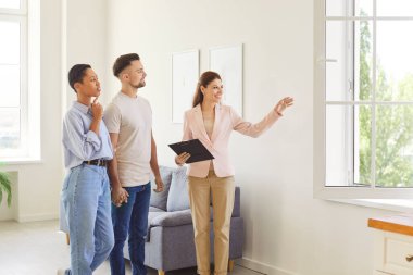 Pencereden manzaraya bakan genç ve mutlu bir çifte ev gösteren kadın emlakçı. Profesyonel emlakçı yeni bir daire gösterdi. Aile ev sahibi olmaya hazır. Emlak kavramı.
