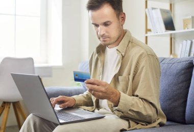 Adam online ödeme için dizüstü bilgisayar ve kredi kartı kullanıyor. Bankacılık bilgilerini doğruluyor ve evdeki kanepede hesap bilgilerine giriyor, dış ticaret ve finans konularına odaklanıyor. İnternet bankacılığı kavramı.