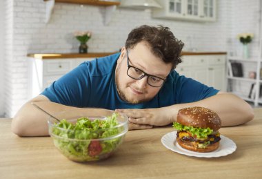 Şişman adam hamburgerle salata seçimini yüzleştiriyor. Evde, beslenme hedeflerini günaha karşı tartıyor ve beslenmesini sorguluyor. Salata sağlıksız bir hamburgere karşı. Basit irade ve seçim teması.