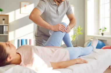 Erkek doktor osteopat ya da fizyoterapist klinikte genç bir kadının dizini muayene ediyor. Hastayla çalışan bir fizyoterapist. Fizyoterapi ve fizik tedavi konsepti.