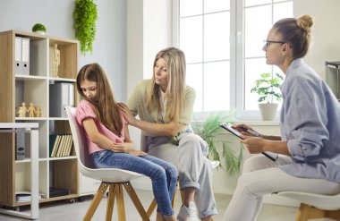 Anne, kız ve psikologla aile terapisi seansı. Danışman, profesyonel bir klinikte rehberlik ve destek sunan odaklı bir konuşma yürütüyor. Açık bir kavram: Aile ruhsal sağlık danışmanlığı.