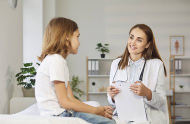Dost canlısı, gülümseyen bir çocuk doktoru çocuk doktorunun portresi klinikteki muayene sırasında koltukta oturan küçük bir çocuk hastayla konuşuyor. Pediatri ve tıp konsepti.