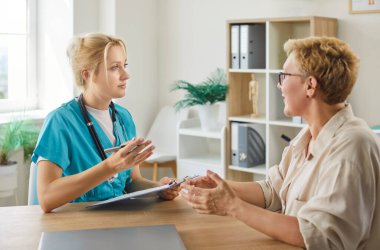 Yaşlı hastalar, tıbbi teşhis ve tedavi planı hakkında konuşmak için klinikteki doktora giderler. Steteskoplu hemşire ve gülümseyen son sınıf öğrencisi danışma masasında oturuyor.