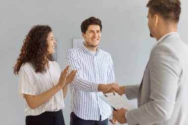 Toplantıda müşteri ve emlakçıların el sıkışması, mutlu çift için yeni bir ev alma ya da kiralama anlaşması. Alıcılar simsar ve gülümseyerek el çırpan kadınla ortaklık anlaşmasını kutluyorlar