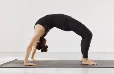 Paspasın üzerinde yoga çarklı asana, arkada derin bir spor salonu. Bir kadının yan görünüşü, kavisli, vücut ve omuzlar, denge ve sabit nefes alış verişi. Kavram: güç, odaklanma, vücut farkındalığı, poz.