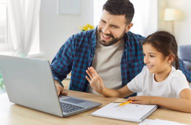 Baba ve kızı dizüstü bilgisayarla birlikte öğreniyorlar. Evde, erkek ebeveyn, kız çocuğa video dersi veriyor, eğitim ve ev ödevlerini destekliyor. Çocukluk. Destekleyici aile eğitimi ve bağlanma.
