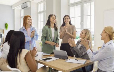 Kadın takım alkışlarla ofiste toplanıyor. İş arkadaşları ve iş adamları başarılı bir anlaşmayı kutlamak için alkışlar ve tezahürat yaparlar. Başarı, kutlama, takım çalışması ve birliği simgeler..