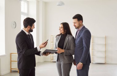 Genç, mutlu, gülümseyen bir çift emlakçıyla anlaşmaya varıyor ve emlak satışı sözleşmesini inceliyor ve kontrat imzalayacaklar. Emlak piyasası ve emlak konsepti satın alma.