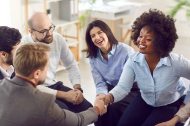 Afrikalı Amerikalı bir kadın başarıyı kutlayan bir adamla el sıkışıyor, anlaşma yapıyor, iş başarısı sağlıyor ya da bir grup insanla iş yerinde bir araya gelip toplantı yapıyor..