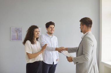 Mutlu müşteriler ve emlakçılar arasındaki el sıkışma ve anlaşmanın başarısı. Gülümseyen çift ve emlakçı, emlak sözleşmesi onaylandıktan sonra el sıkışıyor.