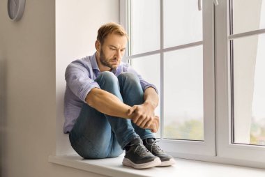 Pencere pencere gezen, düşünen, zihinsel sorunlarla yüzleşen bir adam. Pervaza kıvrılmış, gözleri aşağıda depresyon, endişe, stres, üzüntü ve yalnızlık üzerine kafa yoruyor. Konsept: devam eden zihinsel sağlık mücadelesi.