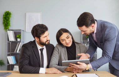 Ofisteki insanlar, çiftler, meslektaşlar masanın etrafında toplanmış tablet bilgisayara dikkatle bakıyorlar, ajan video, resim, bilgi planı veya dijital aygıtla ilgili veri sunuyorlar.