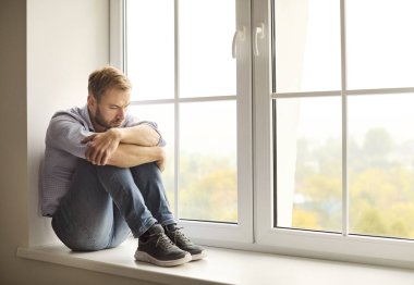 Pencere pencere gezen, düşünen, zihinsel sorunlarla yüzleşen bir adam. Pervaza kıvrılmış, gözleri aşağıda depresyon, endişe, stres, üzüntü ve yalnızlık üzerine kafa yoruyor. Konsept: devam eden zihinsel sağlık mücadelesi.