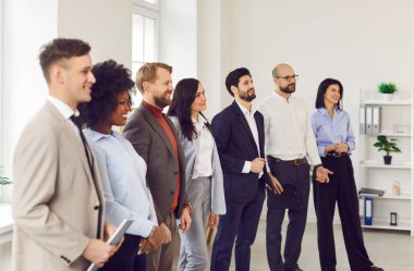 Takım elbiseli bir grup genç iş adamı konferansta sıraya girip meslektaşlarını ya da iş yerindeki liderlerini dinliyor. Şirket çalışanları ofiste toplanıyor.