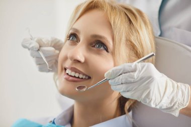 Modern diş hekimliği kliniğindeki kadın hasta portresi. Sağlık merkezindeki sağlık kontrolü sırasında. Dişçi, dişçi aletleriyle genç kadın dişlerini inceliyor. Diş sağlığı hizmetleri.