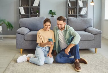 Evde gülümseyen akıllı telefonlar kullanan mutlu bir çift. Gençler birlikte vakit geçirmekten hoşlanıyor. Kadın ve erkek cep telefonu ekranına bakıyor oturma odasındaki koltukta oturuyor. Sosyal medya, aşk kavramı