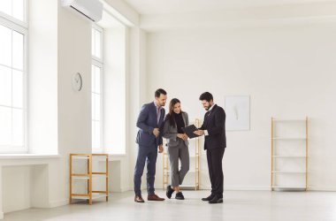 Genç, mutlu, evli bir çift, erkek emlakçıyla belgeleri inceliyor. Aile ev sahibi olmaya hazır. Emlak piyasası ve emlak konsepti.