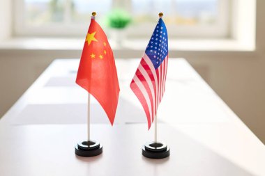 Konferans masasında bayraklar görüşme sinyali veriyor. Çin ve ABD bayrakları karşı karşıya gelerek diplomasi, ikili tartışma ve anlaşma gösteriyor. Tema: Uluslararası diplomasi ve işbirliği.