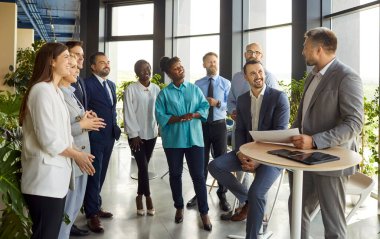 İş adamı, pozitif ofis çalışanlarından oluşan çok uluslu bir ekibin iş toplantısını yönetiyor. Grup arasındaki işbirliği, takım çalışması ve sohbet, iş ve iş dinamiklerine odaklanıyor.