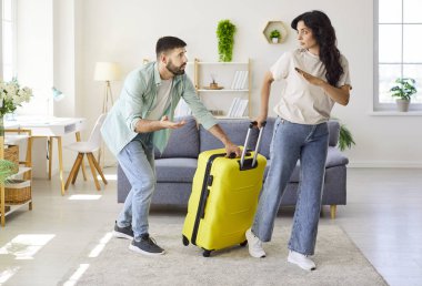 Evde tartışan bir çift. Bavullu üzgün kadın, erkeğin ricası üzerine, modern bir oturma odasında ilişki çatışması, stres ve duygular göstererek ayrılmaya hazırlanıyor. Tema ayrılığı.