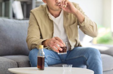 Alkol bağımlısı bir adam evde sigara ve içki içiyor. Sigara bağımlılığı, istismar, depresyon ve sağlık sorunu olan bir bardak ve viski şişesi. Alkolizm sağlığa ve hayata zarar verir.