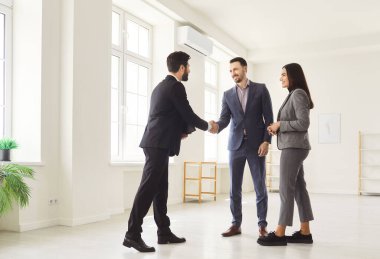 Mutlu gülümseyen genç müşteriler profesyonel bir emlakçıyla el sıkışıyor ve yeni bir dairede emlak almak için anlaşma yapıyorlar. Aile ev sahibi olmaya hazır. Emlak piyasası kavramı