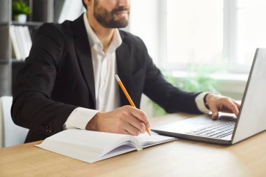 Ofisteki iş adamı dizüstü bilgisayarla deftere yazı yazıyor. Çalışan çalışma masasındaki planları gözden geçirir, notları dengeler ve güneş ışığında bir çalışma alanında bilgisayar araştırması yapar. Konsept planlama, verimli iş akışı.