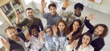 Bir grup mutlu iş adamının üst görüntüsü. Erkekler ve kadınlar kameraya bakıyor, gülümsüyor ve el sallıyorlar. Şirket çalışanları ya da ofiste bekleyen bir grup personel. Pankart.