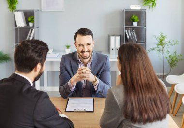 Gülümseyen işadamı ofiste otururken iki kişiyle konuşuyor. Mutlu emlakçı, temsilci ya da mali danışman iş yerinde kadın ve erkek müşterilerle istişarede bulunuyor..