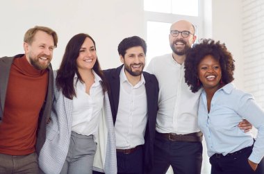 Gülümseyen ve kucaklayan bir grup iş arkadaşı takım çalışması ruhunu ve çeşitliliğini gösteriyorlar. Farklı milletlerden gelen ve içten gülümseyen profesyonel meslektaşlardan oluşan enerjik bir ekibin portresi..