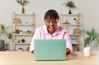 Pozitif ve mutlu Afro-Amerikan kadın internette iyi haberleri dizüstü bilgisayarla aldıktan sonra haykırıyor ve zaferini kutluyor. Heyecan, başarılı bir anı ve kazanmanın heyecanını yansıtır..